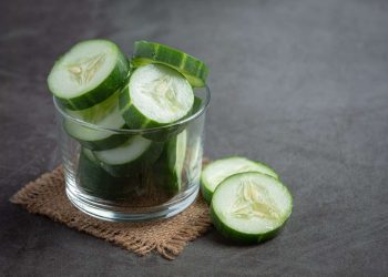 Sliced cucumber slices in a glass bowl on a burlap mat.