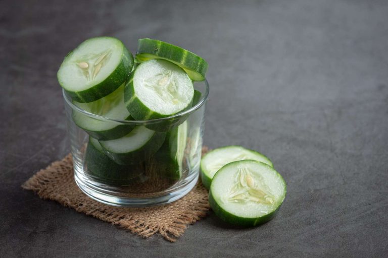 Sliced cucumber slices in a glass bowl on a burlap mat.