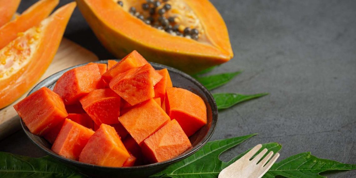 Chopped ripe papaya in a bowl with seeds and leaves on the side.