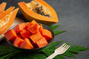 Chopped ripe papaya in a bowl with seeds and leaves on the side.