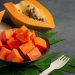 Chopped ripe papaya in a bowl with seeds and leaves on the side.