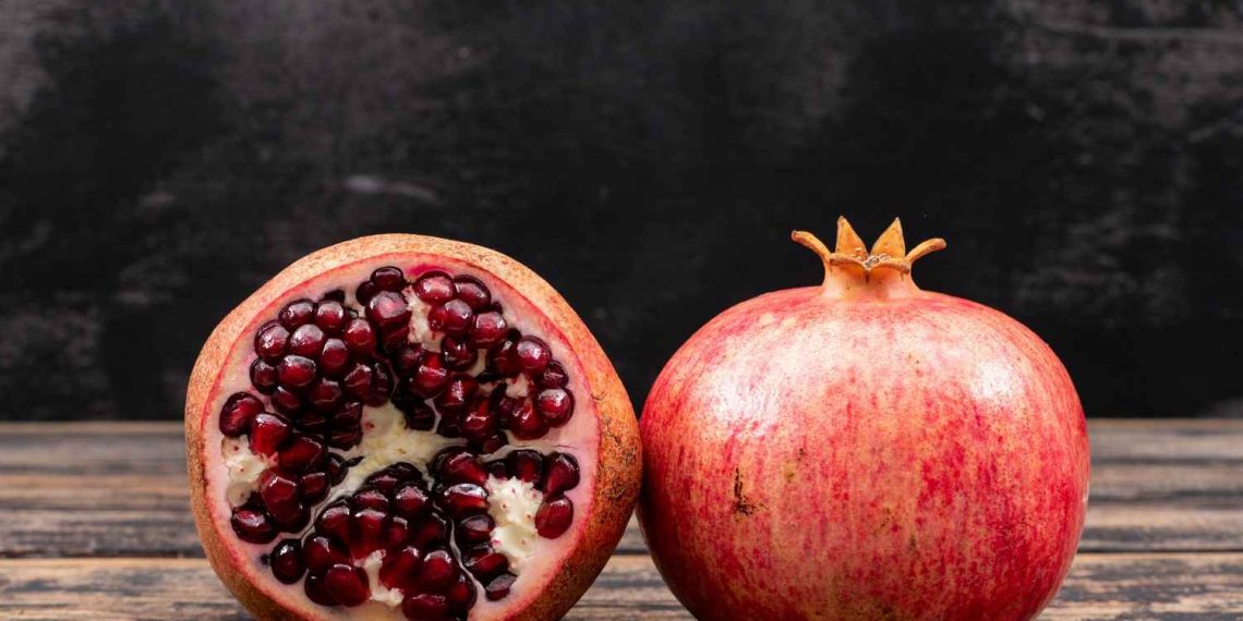 Whole and half pomegranate on wooden table.