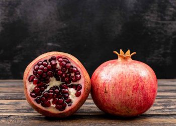 Whole and half pomegranate on wooden table.