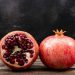 Whole and half pomegranate on wooden table.