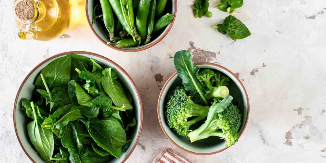 Fresh spinach, peas, and broccoli in bowls on a marble surface.