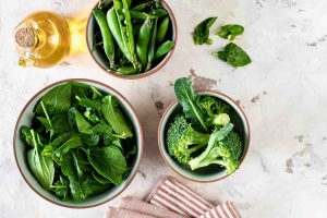 Fresh spinach, peas, and broccoli in bowls on a marble surface.