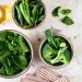 Fresh spinach, peas, and broccoli in bowls on a marble surface.