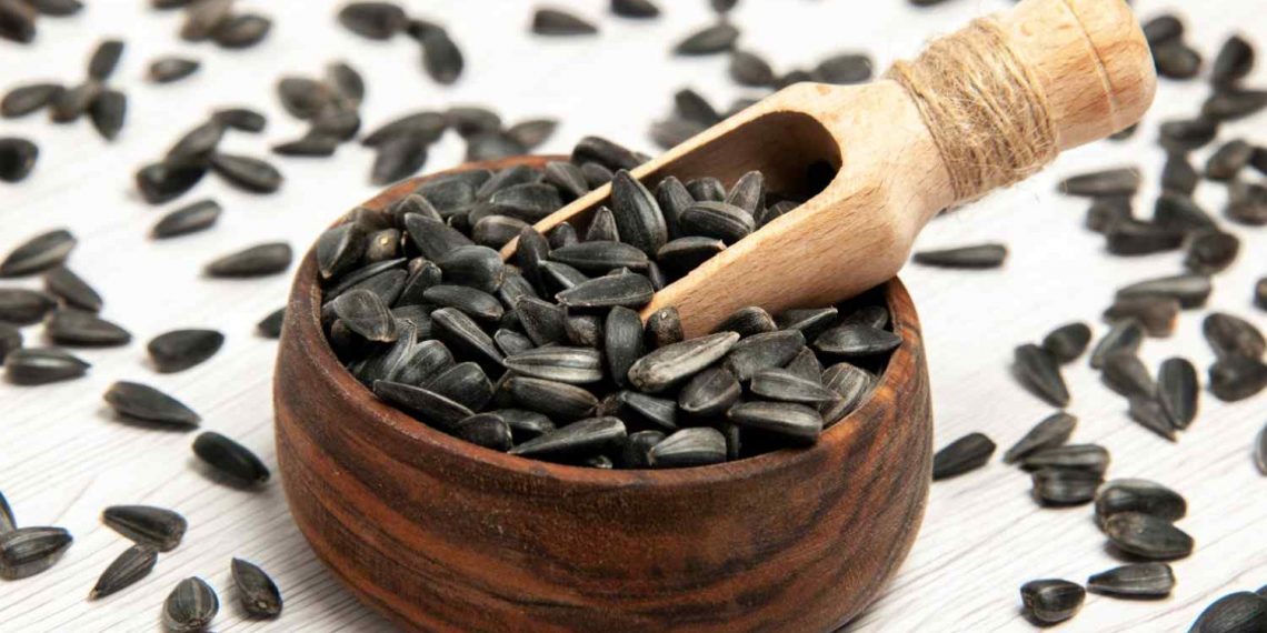 Sunflower seeds in wooden bowl with scooping tool.