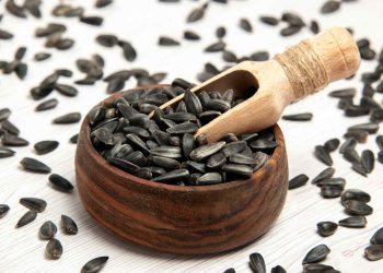 Sunflower seeds in wooden bowl with scooping tool.