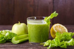 Green juice with apple, celery, lettuce, and lemon on a wooden table.