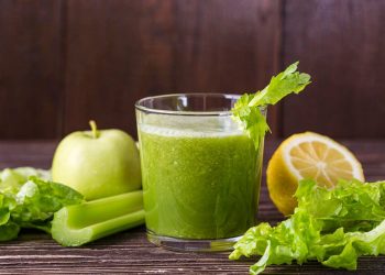 Green juice with apple, celery, lettuce, and lemon on a wooden table.