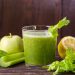 Green juice with apple, celery, lettuce, and lemon on a wooden table.