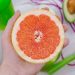 Hand holding a halved grapefruit next to an avocado and a green smoothie.
