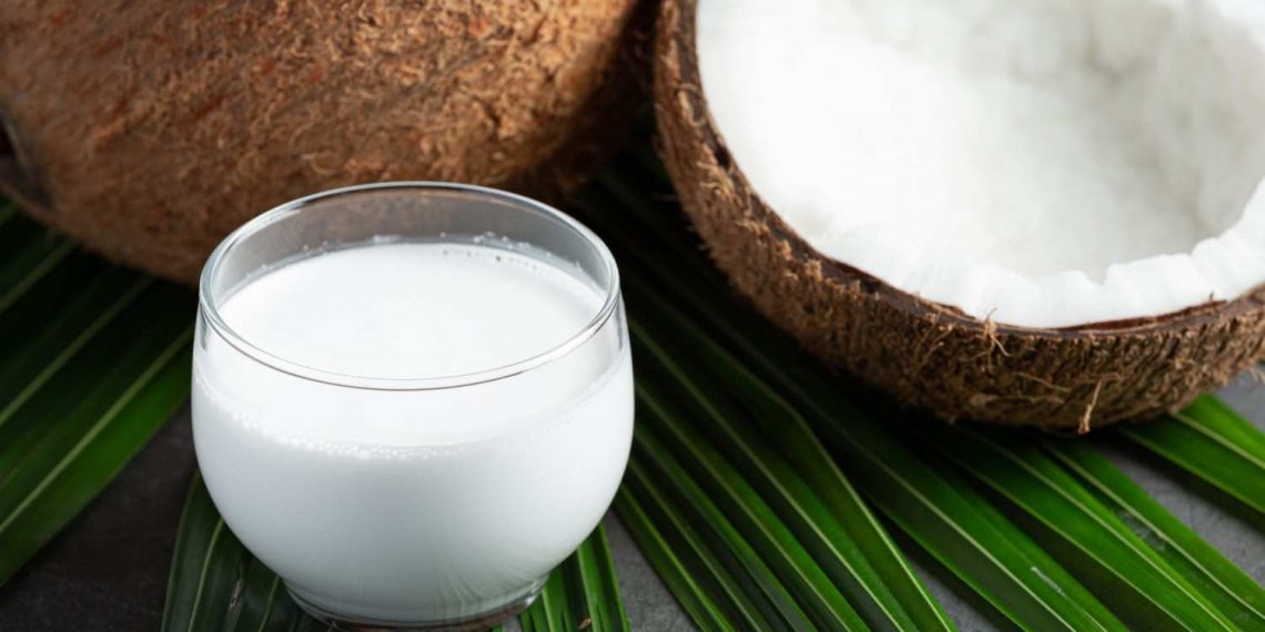 Glass of fresh coconut milk on green leaves.