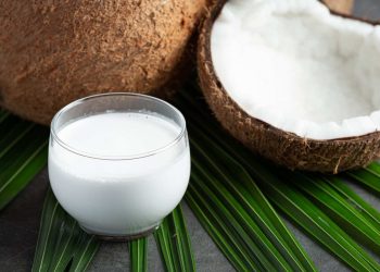 Glass of fresh coconut milk on green leaves.