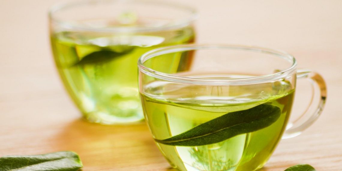 Two cups filled with fresh green tea on a wooden table.