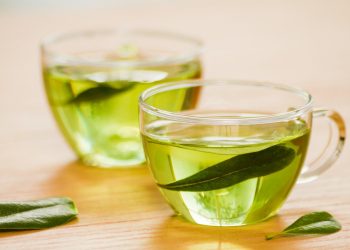Two cups filled with fresh green tea on a wooden table.