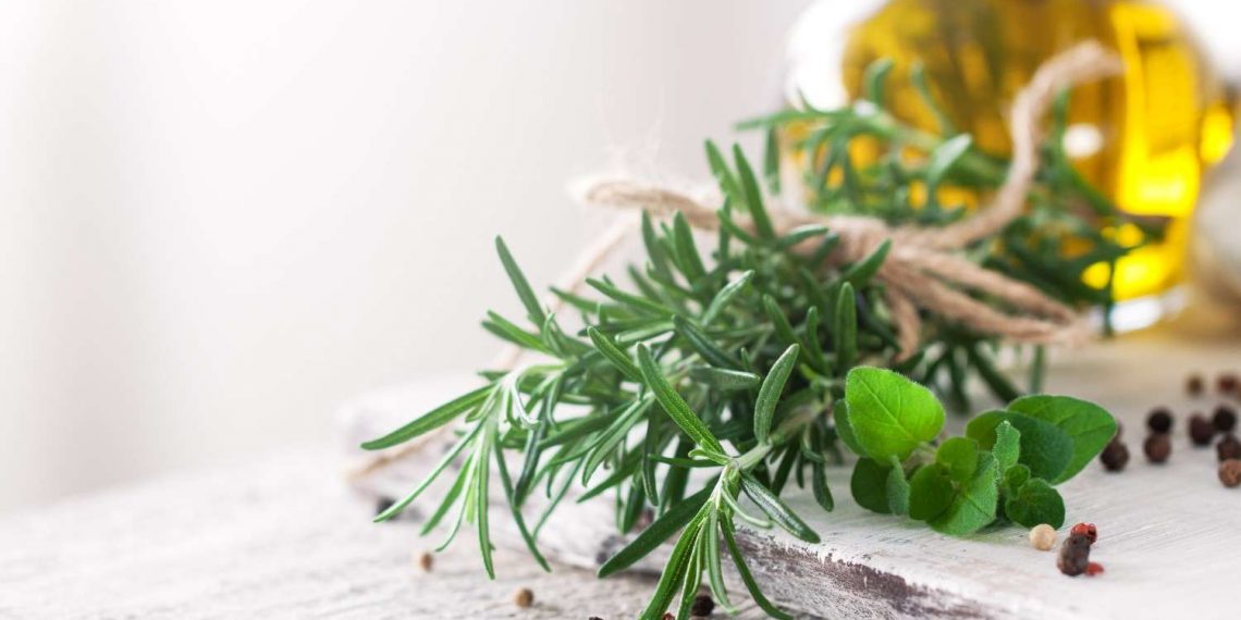 Fresh rosemary and oregano with peppercorns on a rustic table.