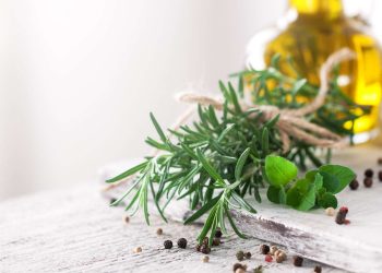 Fresh rosemary and oregano with peppercorns on a rustic table.