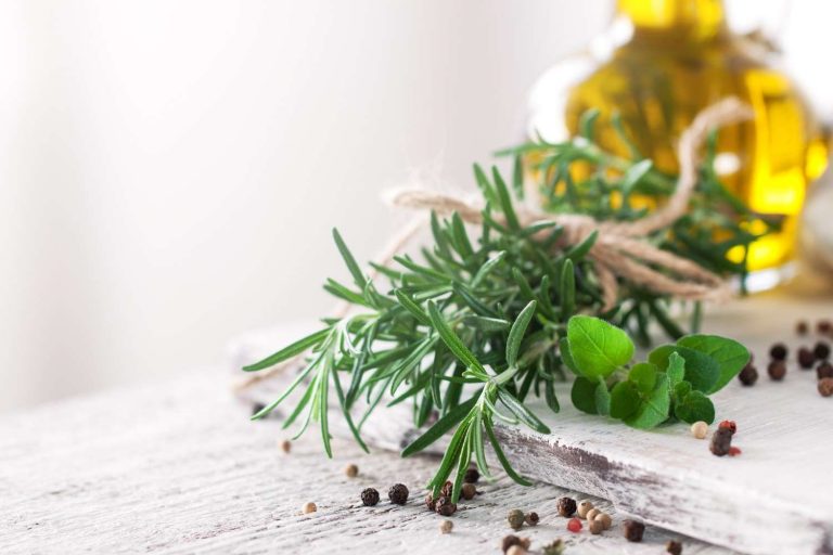 Fresh rosemary and oregano with peppercorns on a rustic table.