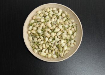 Jasmine buds in a bowl on dark table surface.