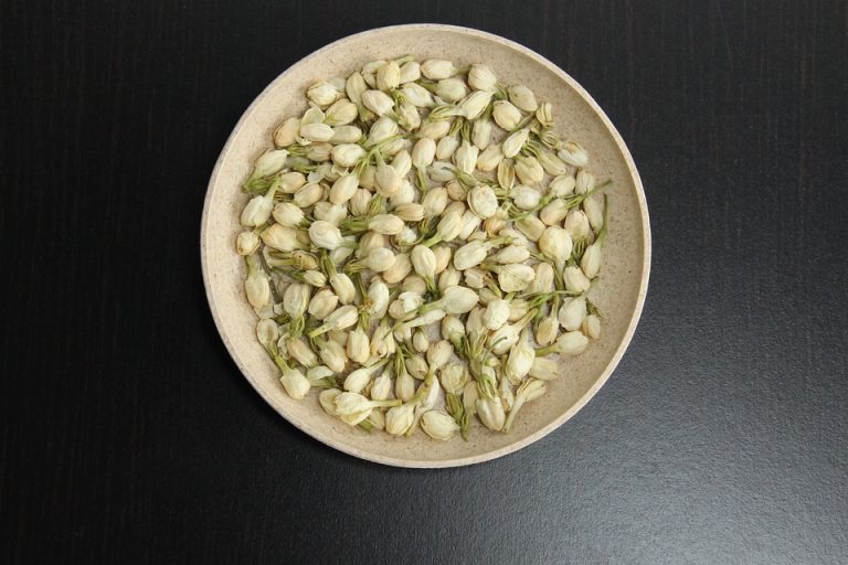 Jasmine buds in a bowl on dark table surface.