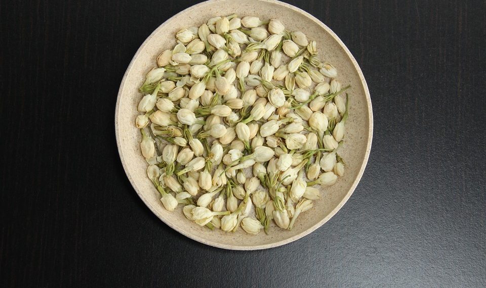 Jasmine buds in a bowl on dark table surface.