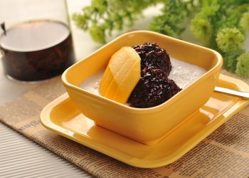 Creamy dessert with mango slices and black rice in a yellow bowl.