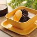 Creamy dessert with mango slices and black rice in a yellow bowl.