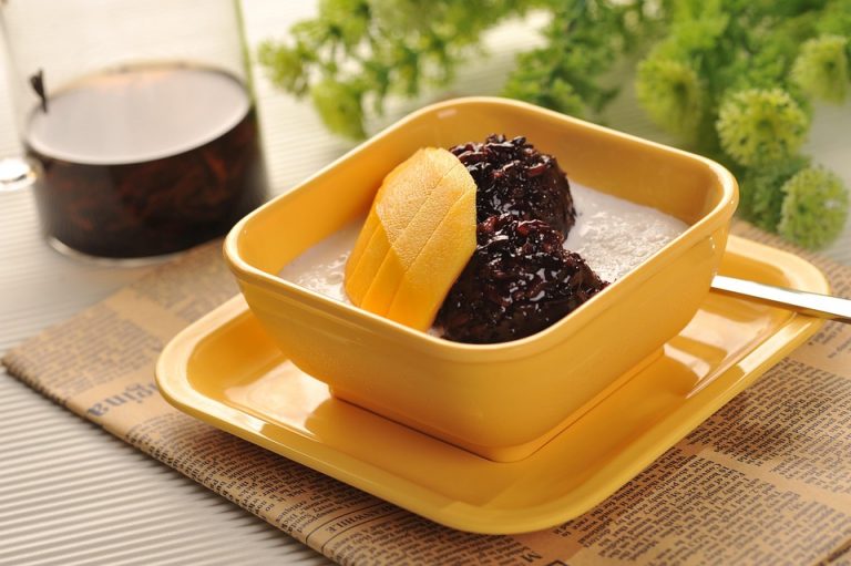 Creamy dessert with mango slices and black rice in a yellow bowl.