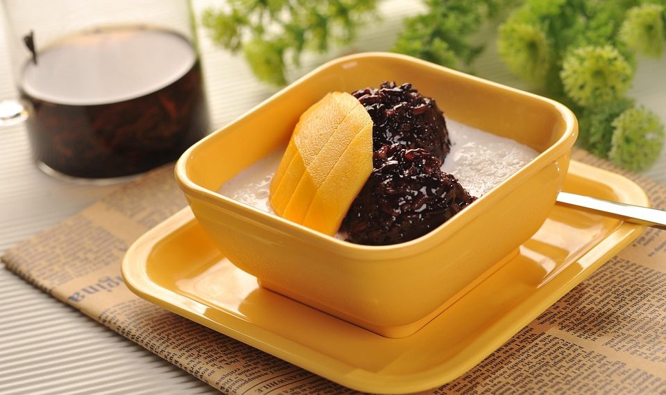 Creamy dessert with mango slices and black rice in a yellow bowl.