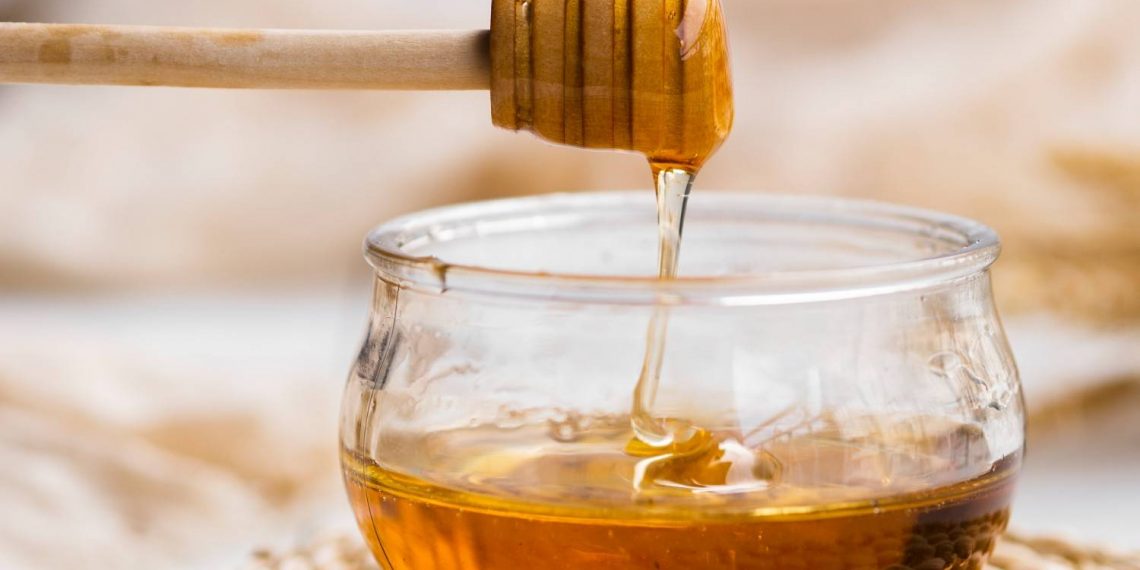 Drizzling honey from dipper into a glass jar.
