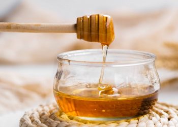 Drizzling honey from dipper into a glass jar.