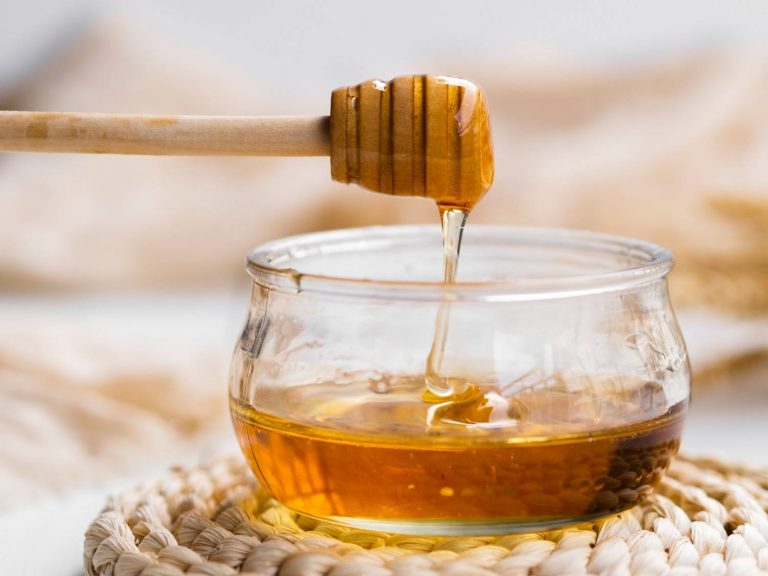 Drizzling honey from dipper into a glass jar.
