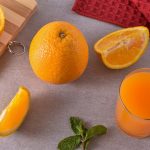 Fresh oranges and juice on a kitchen counter with mint leaves and a red towel.