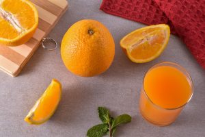 Fresh oranges and juice on a kitchen counter with mint leaves and a red towel.