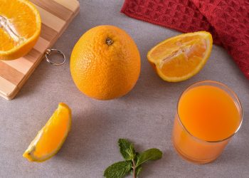 Fresh oranges and juice on a kitchen counter with mint leaves and a red towel.