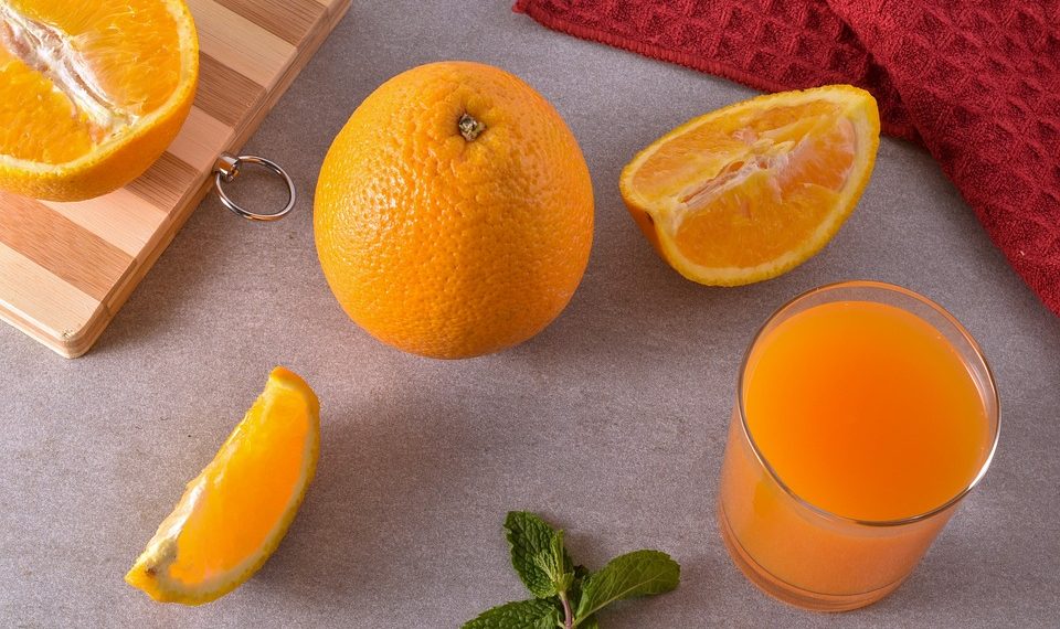 Fresh oranges and juice on a kitchen counter with mint leaves and a red towel.