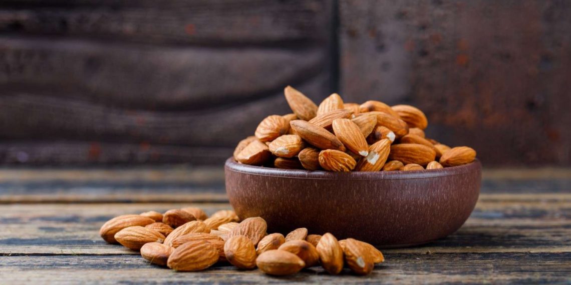 Bowl of raw almonds on rustic wood table.