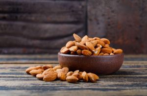 Bowl of raw almonds on rustic wood table.