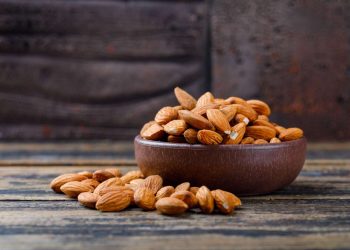 Bowl of raw almonds on rustic wood table.