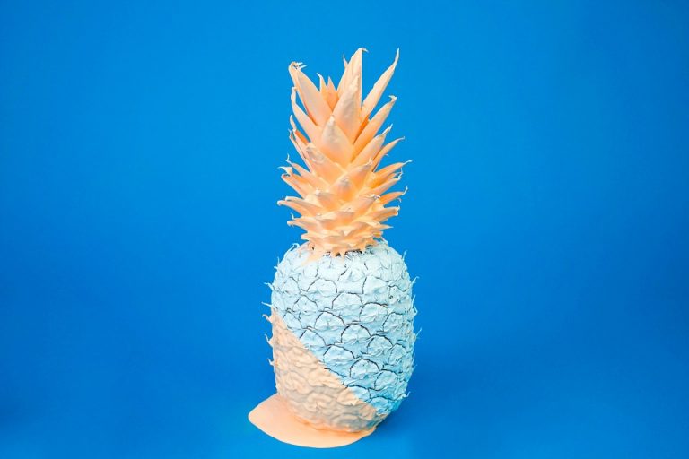 Unique pastel-painted pineapple against a blue background.