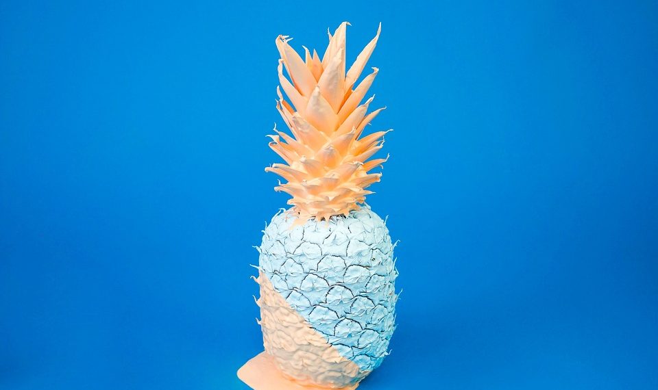 Unique pastel-painted pineapple against a blue background.