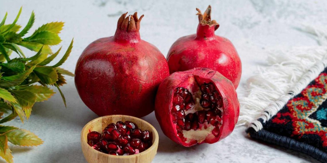 Pomegranates and seeds in a bowl on a table with a decorative cloth.