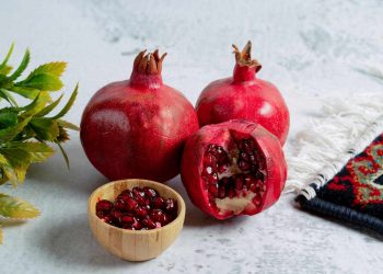 Pomegranates and seeds in a bowl on a table with a decorative cloth.
