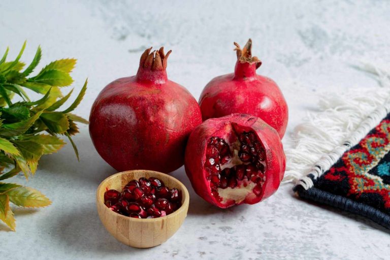 Pomegranates and seeds in a bowl on a table with a decorative cloth.