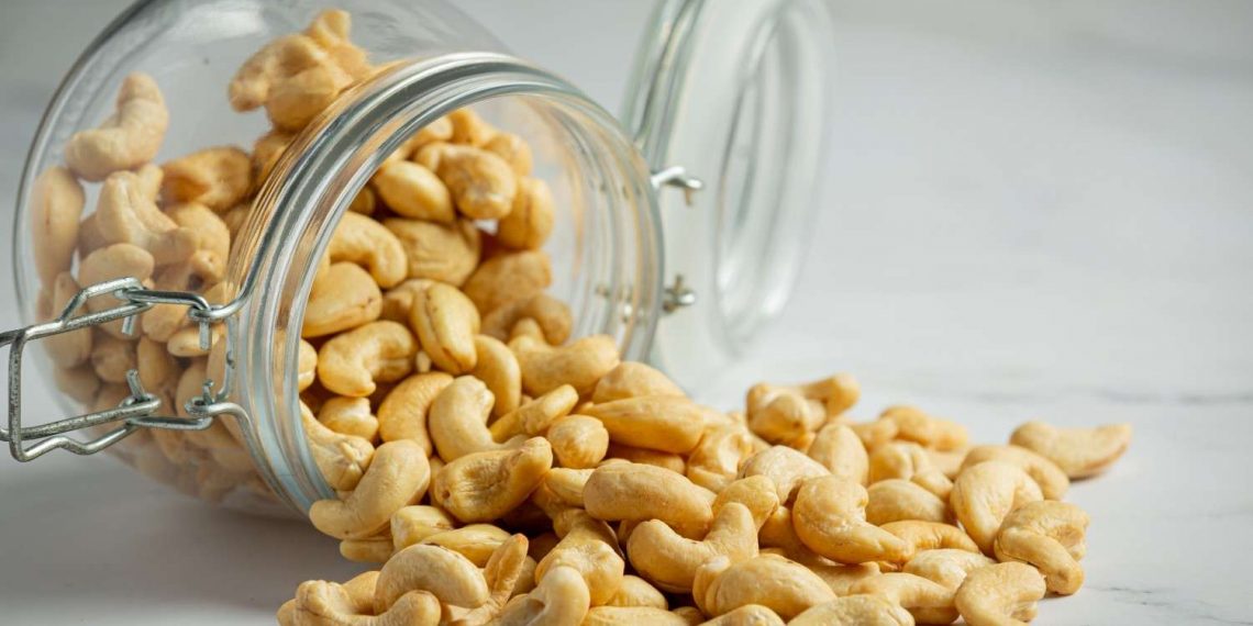 Cashews spilling from a glass jar on a marble surface.