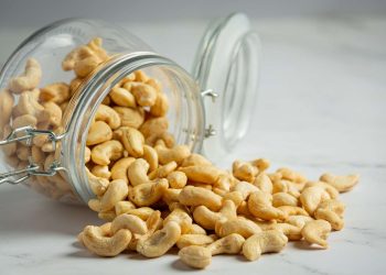 Cashews spilling from a glass jar on a marble surface.