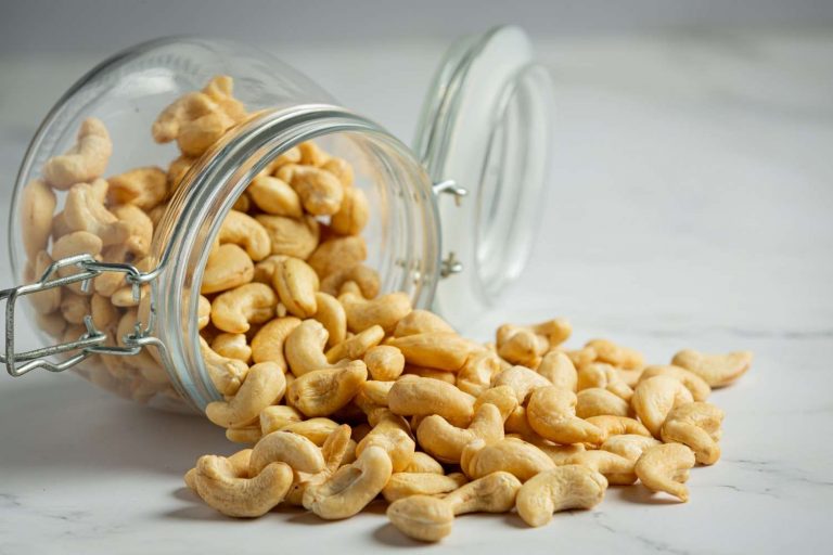 Cashews spilling from a glass jar on a marble surface.