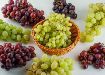 Mixed grapes arranged around a wicker basket on white background.